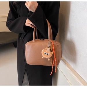 Detail of brown lychee grain leather bag with lion plush pendant and brand engraving