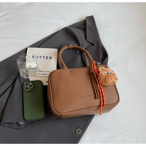 Brown litchi grain leather handbag with plush monster charm on grey suit jacket