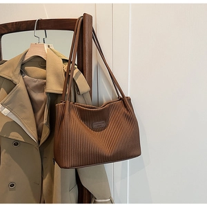 Detail of the pleated texture and brand plaque on a coffee brown faux leather tote bag