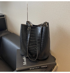 Detail of black crocodile embossed leather bucket bag with adjustable metal buckle strap