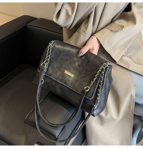 Detail of a vintage black crossbody bag with gold chain strap worn with a trench coat