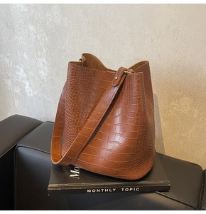 Detail of caramel brown croc-embossed bucket bag with metallic hardware and leather strap