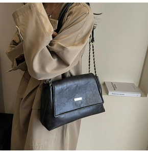 Detail of a vintage black leather crossbody bag with gold hardware on khaki trench coat