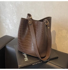 Detail of dark brown crocodile texture bucket bag with gold hardware on book background