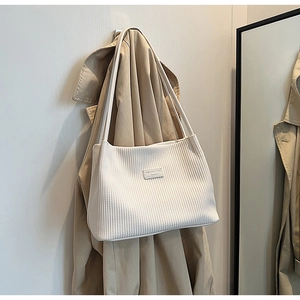Close-up of white pleated tote bag with fashion tag hanging on a stylish khaki coat