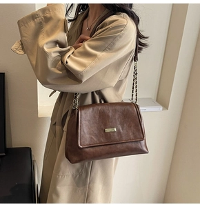 Detail of vintage brown leather bag with gold metal plate and chain strap on a trench coat