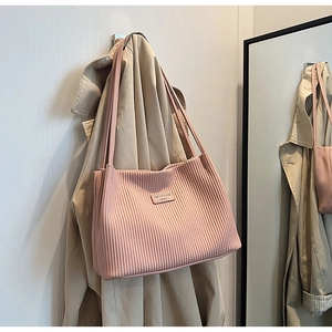 Detail of pink pleated knit tote bag showing vertical texture and metal logo plate