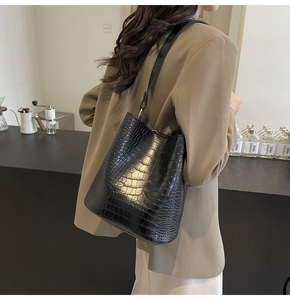 Detail of black crocodile texture bucket bag worn by model in minimalist cafe setting