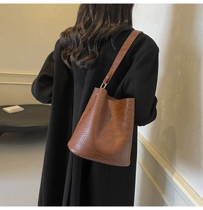 Brown crocodile embossed bucket bag with gold hardware worn by a model in a minimalist setting