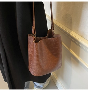 Detail of a brown crocodile pattern bucket bag with golden hardware on a model