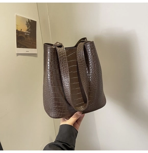 Detail of dark brown crocodile embossed bucket bag featuring wide shoulder strap design