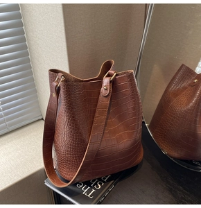Detail of brown crocodile pattern bucket bag with wide strap and golden hardware