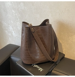 Detail of dark brown crocodile-embossed bucket bag with wide strap and gold hardware