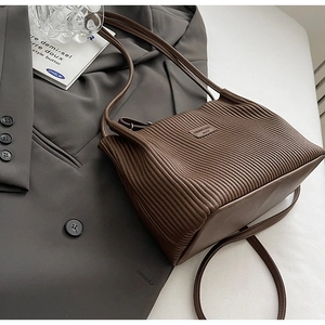 Detailed close-up of dark brown pleated bucket bag on a grey blazer suit jacket