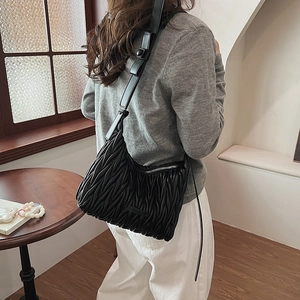 Close-up of black pleated texture on crossbody bag with adjustable leather shoulder strap