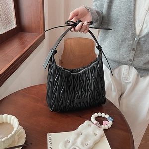 Detail shot of black matelassé textured shoulder bag with metallic logo and zipper closure