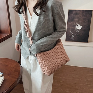 Detail of pink pleated crossbody bag featuring a cute bow on the strap and metal plaque