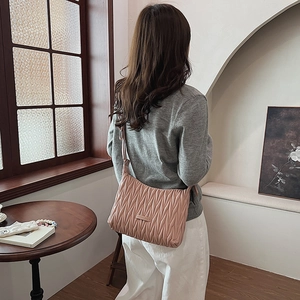 Detail of pink Matelassé pleated shoulder bag with fashion metal logo on textured surface