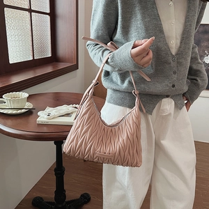 Detail of light pink pleated hobo bag with adjustable strap on a vintage wooden table
