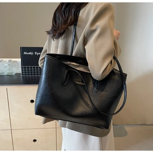 Detail of a large black PU leather tote bag with long straps worn on the shoulder by a model