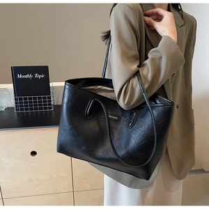Close-up of a large black tote bag featuring a square logo and premium leather texture