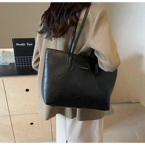 Detail of black leather tote bag featuring golden lettering and fine pebble texture