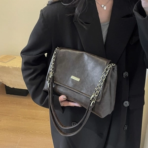 Retro dark brown crossbody bag with gold buckle and chain strap on a black blazer