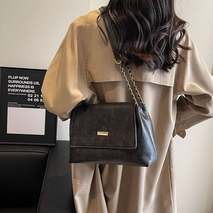 Retro black leather shoulder bag with gold metal buckle and chain strap on a model