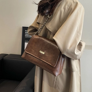 Vintage brown crossbody bag with gold buckle and chain strap shown on a beige trench coat