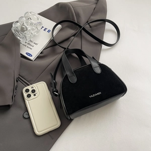 Mini black crossbody bag detail showing matte texture and leather handle on a grey suit