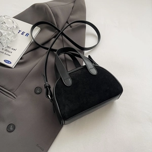 Detail of a black matte Boston bag styled on a grey blazer with minimalist decor