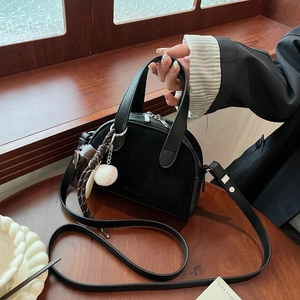 Detail of black semi-circular bag showing matte texture and baseball charm with silver zipper