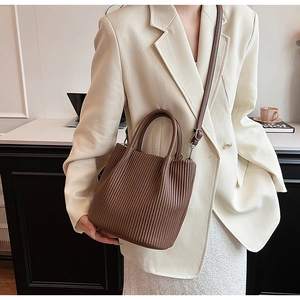 Close-up of brown pleated bucket bag with dual handles and thin shoulder strap details