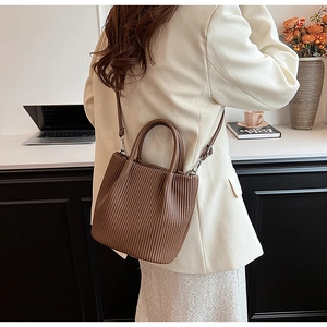 Detail of a pleated dark brown bucket bag featuring dual handles and a detachable strap