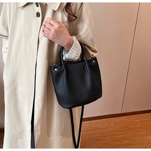 Detail of a black pleated bucket bag with vertical texture and golden hardware