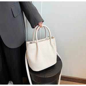 Close-up of white pleated bucket bag with dual ring handles and silver metal hardware