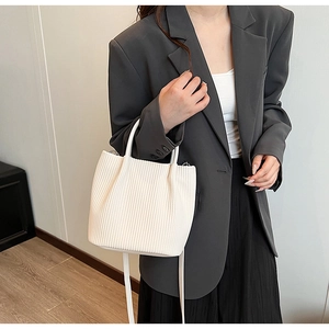 Detail of white pleated bucket bag with long shoulder strap in a minimalist room
