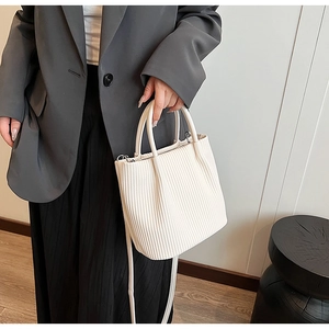 Detailed view of cream pleated bucket bag with vertical textures and slim shoulder strap