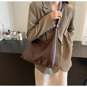 Detail of a dark brown crescent tote bag worn by a model in a professional office setting