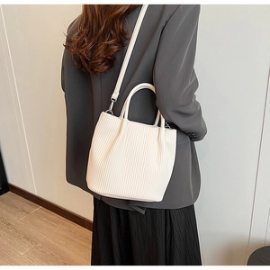 Detailed view of white pleated bucket bag texture with silver hardware on grey blazer