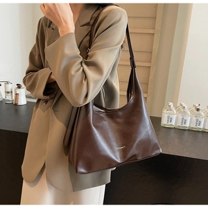 Detail of a dark brown glossy underarm bag with silver logo on a khaki suit