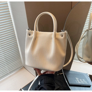Detail of off-white pleated bucket bag with textured vertical folds and sturdy top handles