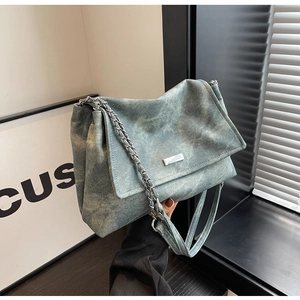 Detail of washed denim chain bag showing vintage faded texture and metal logo plaque