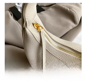 Detail of smooth gold zipper and embossed logo on beige lychee leather handbag