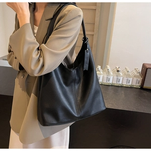 Close-up of black lychee grain leather tote bag with vertical stitching and luggage tag