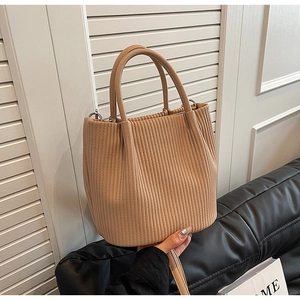 Detailed close-up of beige pleated bucket bag with vertical texture on black leather sofa