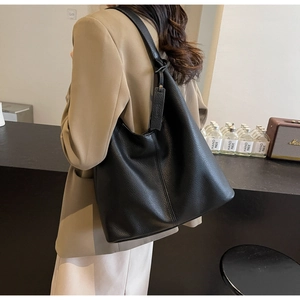 Detail of a black pebbled leather hobo tote bag with a wide shoulder strap worn by a model