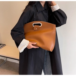 Detail of caramel brown leather clutch with oval silver handle and embossed logo