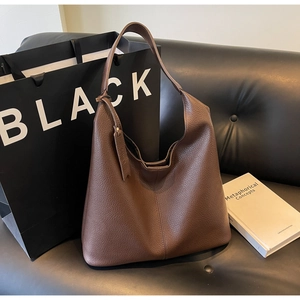 Detail of brown lychee texture leather tote bag with stylish knot strap on leather sofa