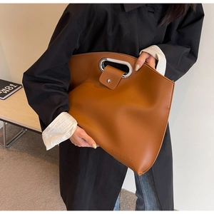Detail view of large brown leather tote with circular silver handle and embossed logo